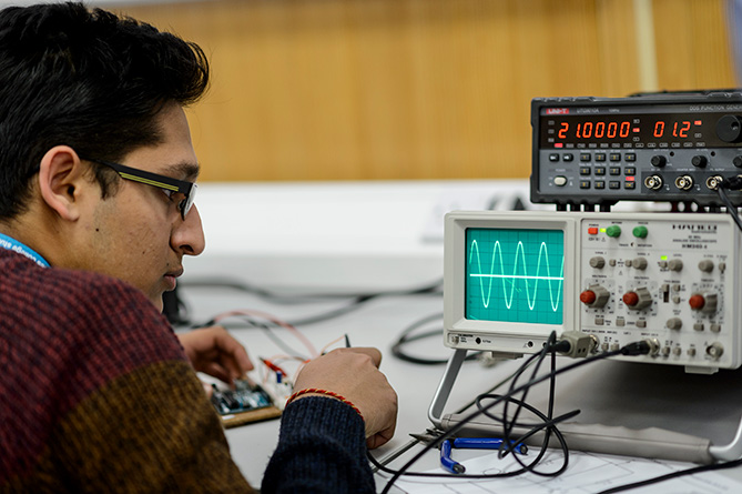 A young man tunes an electrical circuit achieving a perfect sinusoidal current on an oscilloscope